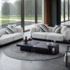 Modern living room with white curved sofas a dark coffee table and a circular rug by floor to ceiling windows showing an outdoor view of trees and water