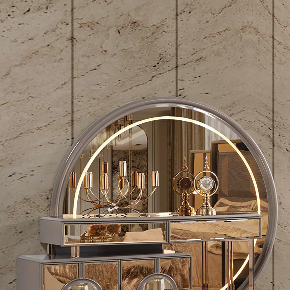 Round, backlit mirror atop a mirrored vanity with gold accents and drawers in a luxurious room.