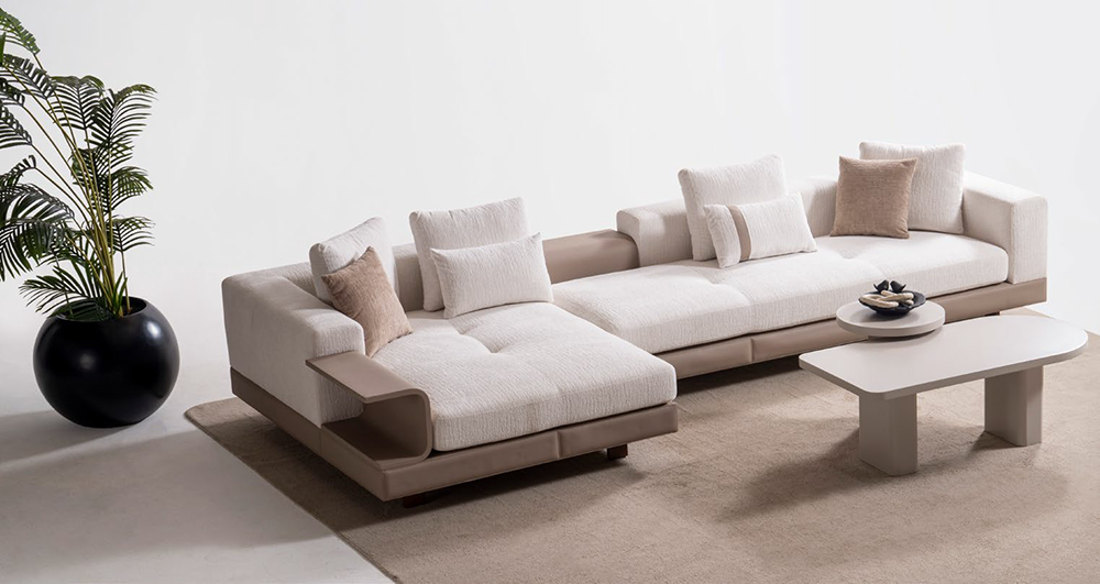 Modern L-shaped sectional sofa with cream cushions and tan armrests in a minimalist living room with a potted plant nearby.