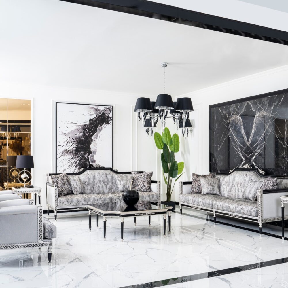 Luxurious living room with silver ornate sofas, black chandelier, and black-and-white artwork against marble floors.