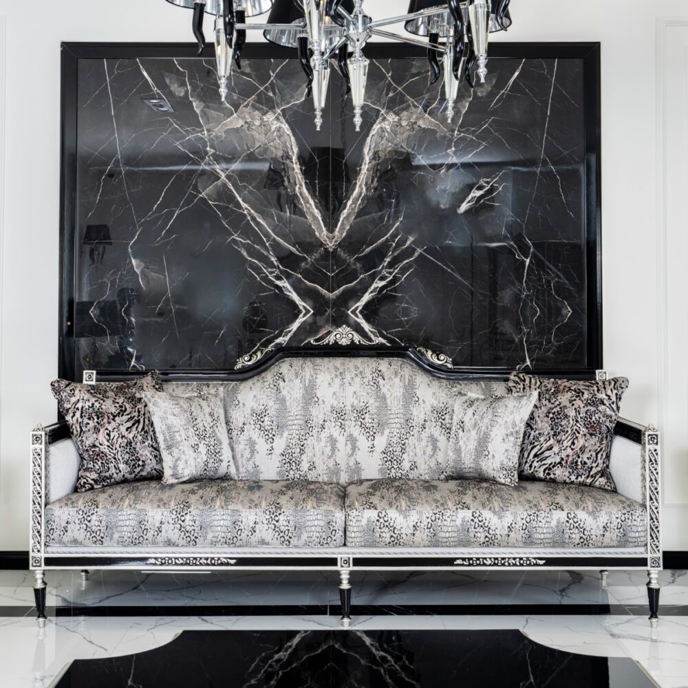 Luxurious living room with a black marble panel wall, ornate silver-framed snakeskin-patterned sofa, and a crystal chandelier overhead.