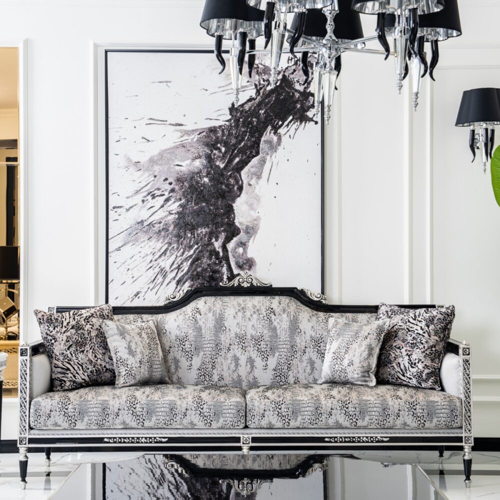 Luxurious black-and-silver sofa with animal-print cushions in a bright white living room, featuring a large monochrome abstract painting, chandelier, and tall green plant.