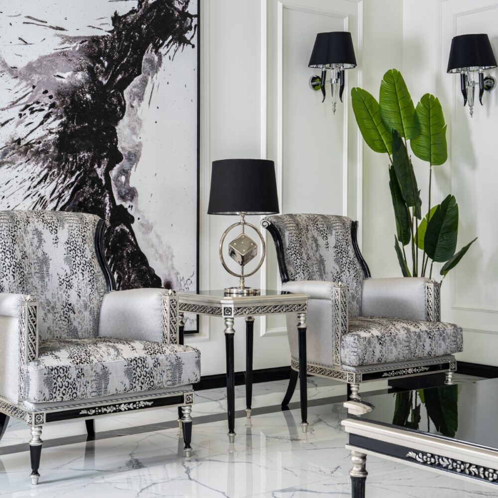 Luxurious living room with silver-and-leopard-print chairs, a matching glass-topped table, black lamps, a large abstract black-and-white painting, and a tall green plant against paneled white walls.