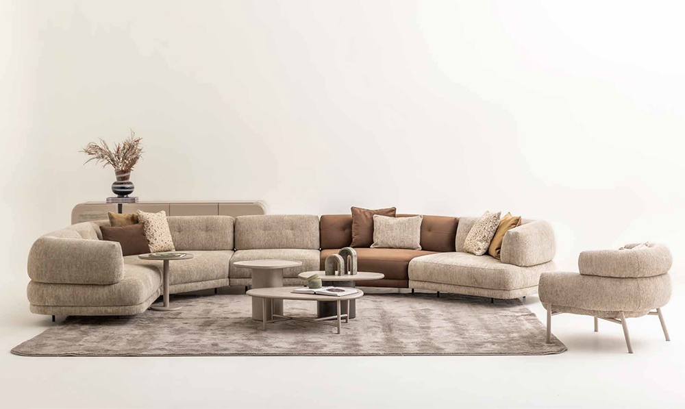 Cream/beige sectional sofa with cushions in a bright minimalist living room, centered on a gray rug and low tables.