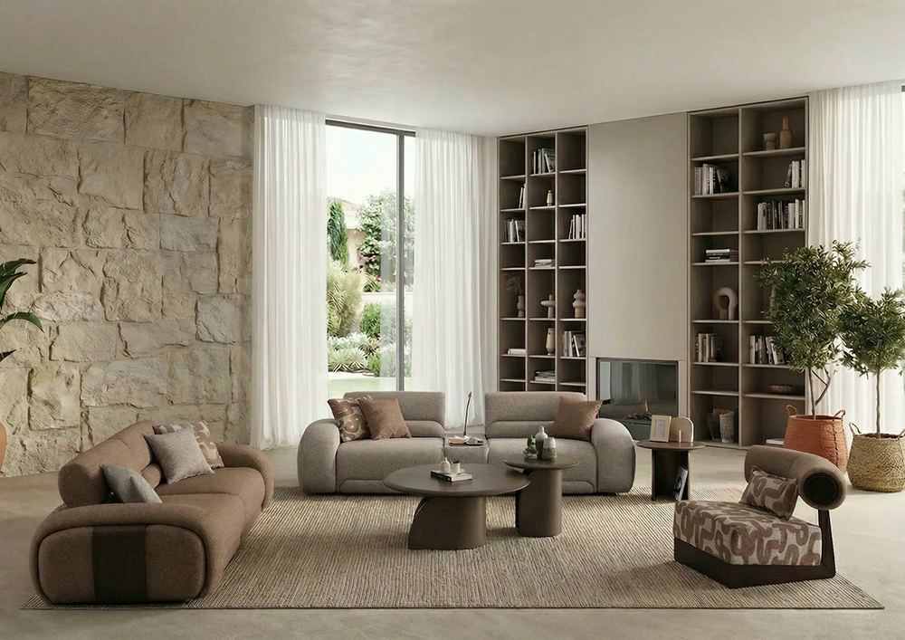 Contemporary living room with neutral sofas, a textured stone wall, and tall built-in bookshelves flanking a fireplace. Large windows with sheer curtains bring in natural light.