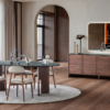 Round dining table with four cushioned chairs on a light rug in a modern dining area with wood floors and large windows with sheer curtains