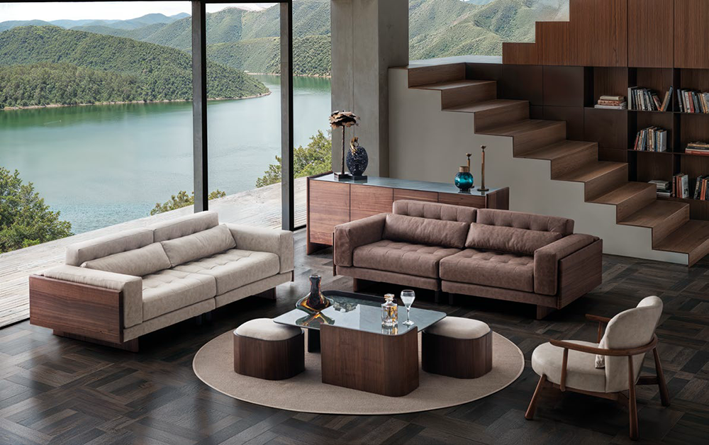 Modern living room with floor-to-ceiling windows overlooking a lake and mountains, two sofas, and a glass coffee table.
