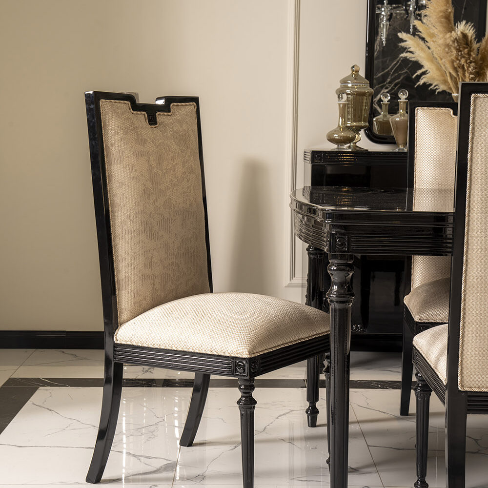 Elegant dining set with black wooden chairs and beige upholstered seats around a glossy black table on a marble floor, with a decorative mirror and dried pampas grass in the background
