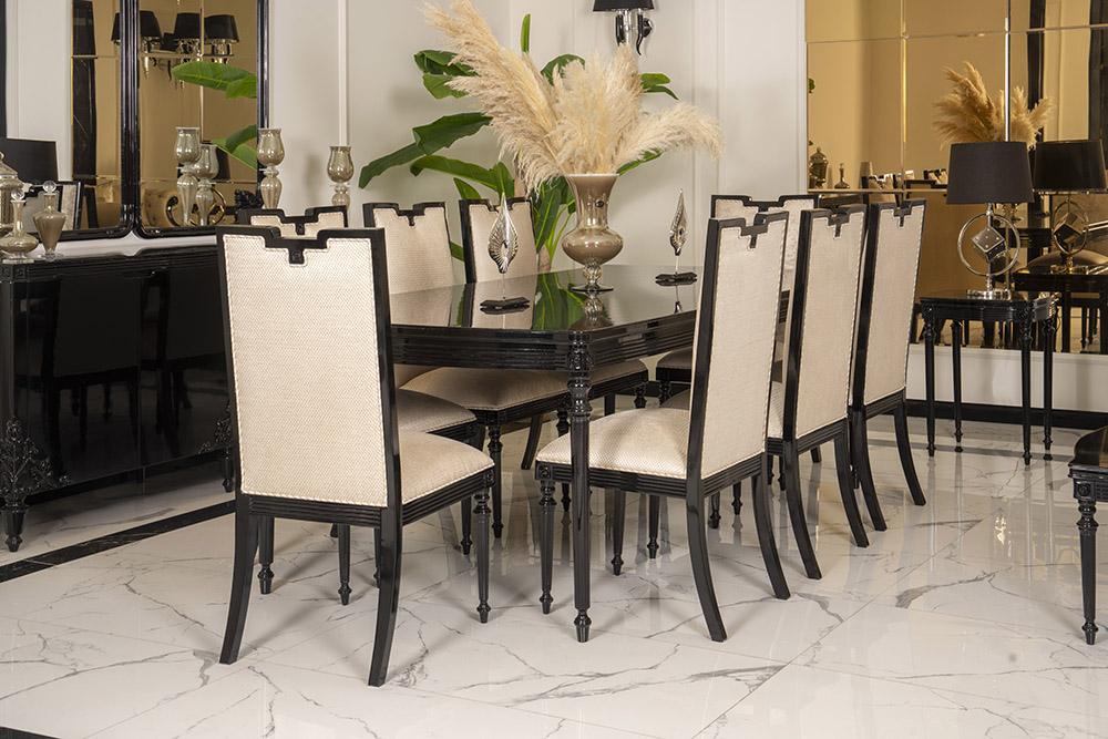 Elegant dining room with a long black table and beige upholstered chairs, pampas grass centerpiece on a marble floor.