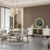 Modern dining room with a white oval table upholstered chairs and a beige rug under a stylish pendant light A white sideboard with a round backlit mirror sits on a taupe wall