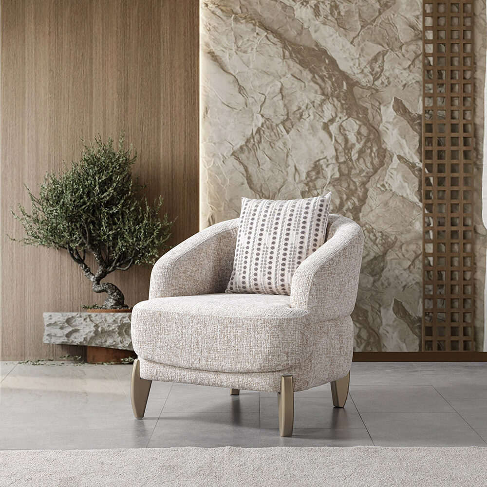 Creamy upholstered curved armchair with a patterned throw pillow in a modern stone-walled room, next to a small bonsai plant and wooden paneling.