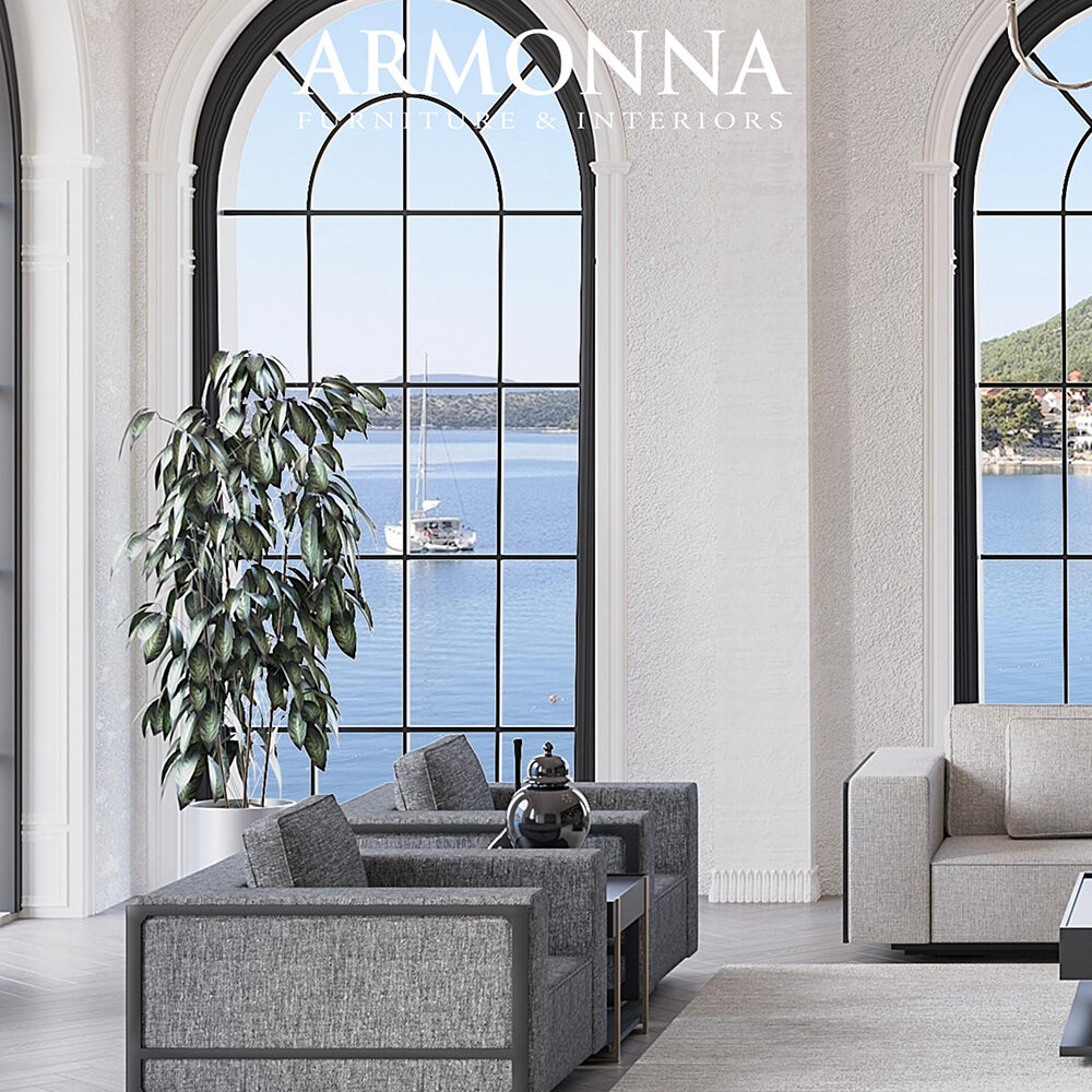 Modern living room with gray sofas, a tall plant, and large arched windows overlooking a lake; Armonna Furniture & Interiors logo.