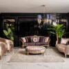 Luxurious living room with mauve velvet sofas gold trim and a tufted round ottoman under a blue shaded chandelier