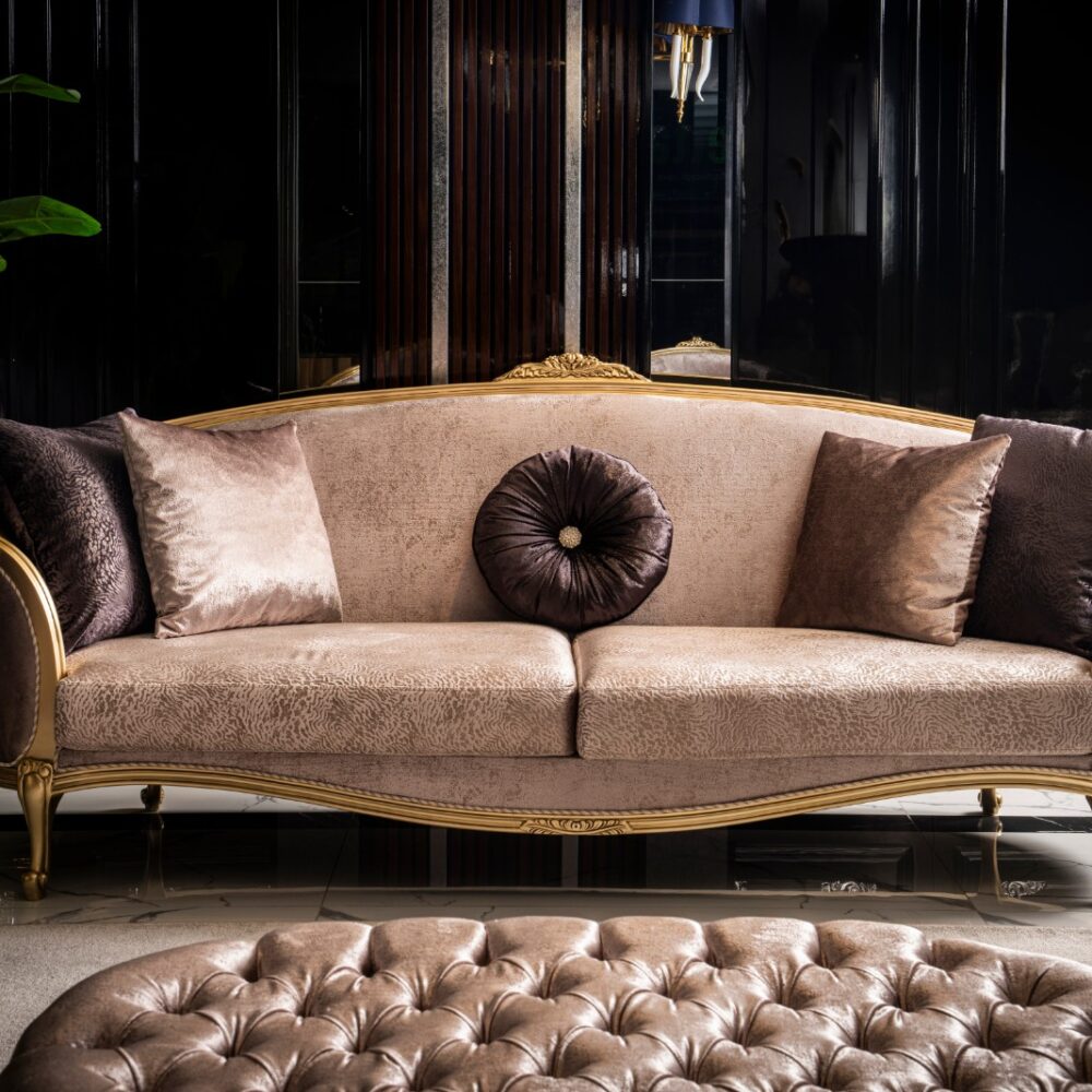 Luxurious beige sofa with a gold frame and velvet cushions in a dark, glossy interior.