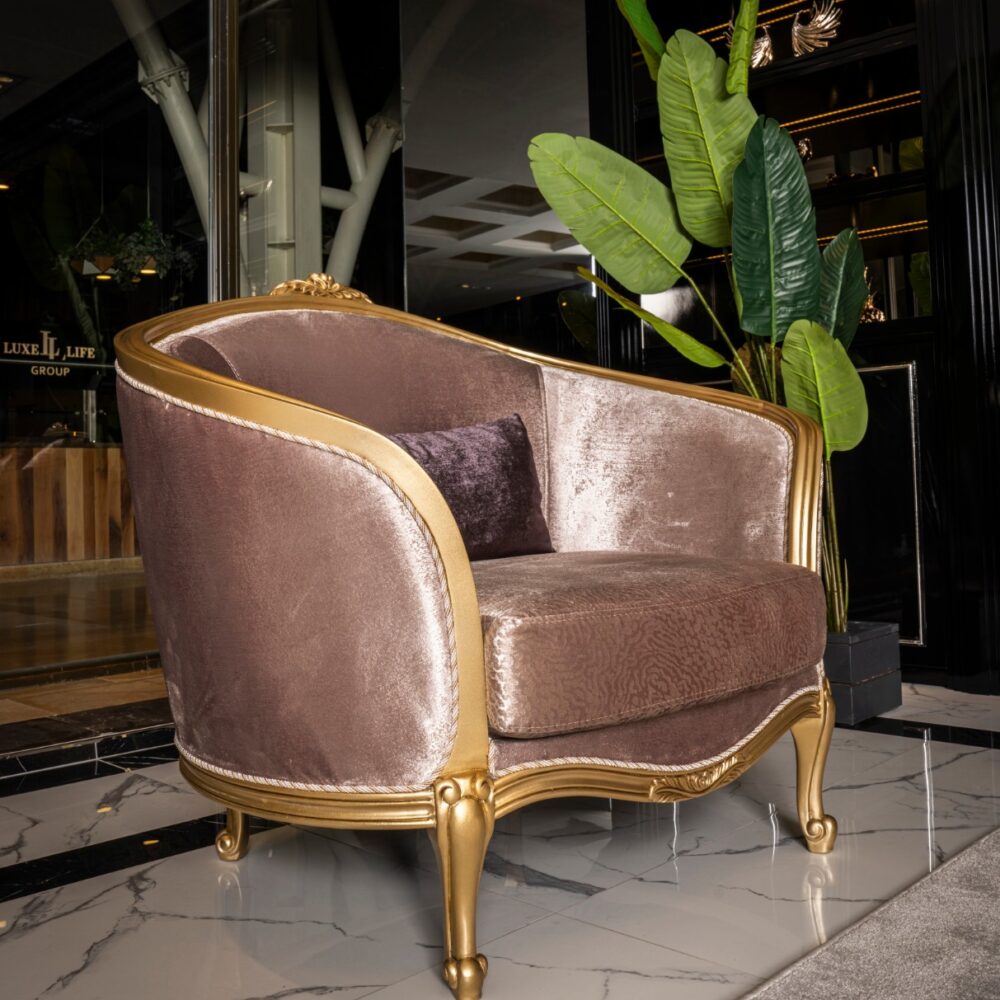 Luxurious pink velvet armchair with a gold frame and carved details in a marble-floored lobby, with a large green plant nearby.