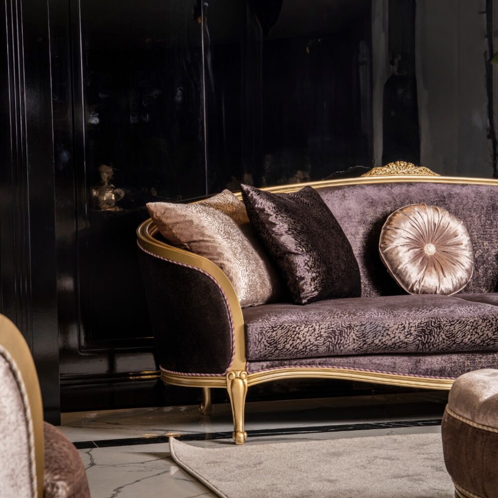 Luxurious velvet purple sofa with gold trim and matching cushions in a dark, glossy room, with green plants nearby.