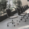 Row of black swivel chairs with metal bases and wheels along a long conference table in a bright plant filled workspace