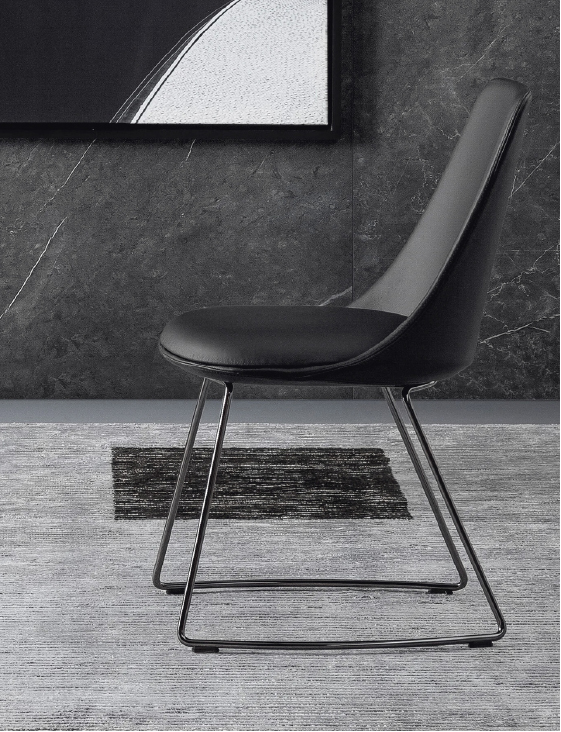 Black upholstered chair with metal sled legs in a modern room with a dark textured wall behind it.