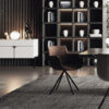 Modern lounge area with a dark shelving unit filled with books and decorative pieces a brown chair and a round table on a striped rug