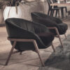 Two black upholstered lounge chairs with wooden frames on a stone patio near potted plants and a dining table in the background