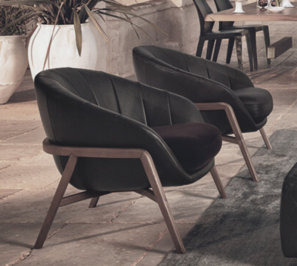 Two black upholstered lounge chairs with wooden frames on a stone patio, near potted plants and a dining table in the background.
