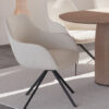 Modern white upholstered chair with black metal legs beside a round wooden table in a bright minimalist room