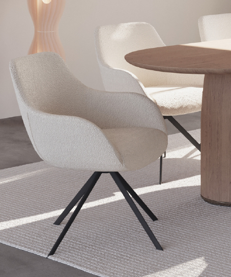 Modern white upholstered chair with black metal legs beside a round wooden table in a bright, minimalist room.
