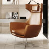 Brown leather swivel lounge chair with tall back in a modern tiled room setting with shelves behind it