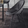 Gray curved lounge chair with slender metal legs beside a glass table in a modern office setting on a dark rug