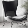 Modern high back lounge chair with curved seat and slim metal legs in a bright living room with vertical blinds and a plant nearby