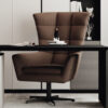 Brown upholstered swivel desk chair at a black desk in a modern home office with books and decor on a shelf behind