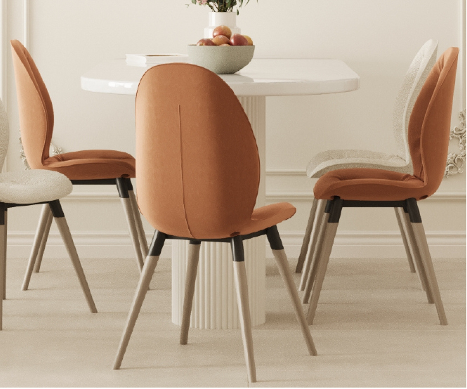 Four orange and beige dining chairs around a white round table with a fruit bowl in a bright, minimalist dining room.