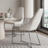 Bright dining area with beige upholstered chairs around a round white table a plant centerpiece and a large window view