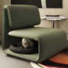Cat comfortably naps inside the hollow of a green modern lounge chair in a living room setting with a side table and magazines nearby