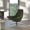 Green mid century lounge chair with a metal four point base in a sunlit living room by a fireplace and coffee table