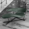 Green leather lounge chair with a metal X base in a modern living area beside a brick wall and staircase