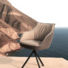 Modern cushioned outdoor chair on a terrace with rocky coastline and sea in the background daylight soft pink tones