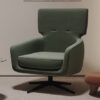 Green upholstered swivel armchair with curved arms placed on a beige carpet in a neutral room with wall art above