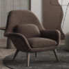 Brown upholstered armchair with a matching cushion standing on a round dark rug in a modern living space with wooden legs