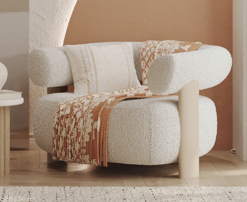 Cream boucle armchair with rounded arms and a warm orange-brown throw draped over it, in a sunlit living room setting.