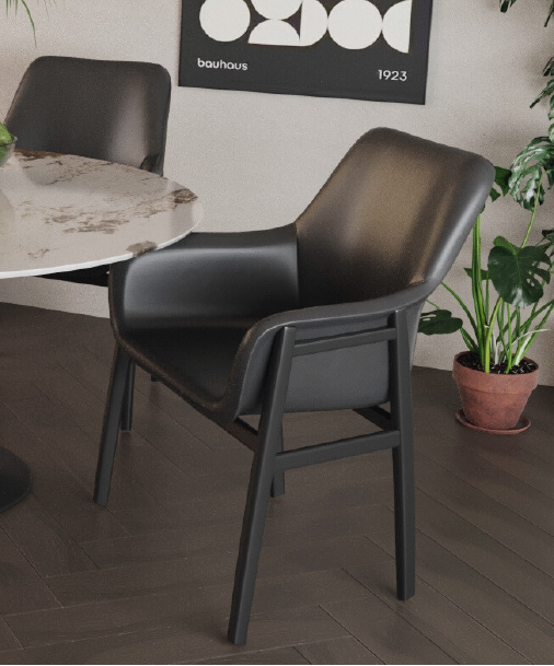 Black modern armchair with curved back and armrests beside a round marble table in a contemporary office space with potted plants in the background