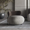 Round ottoman with gray geometric pattern and a dark brown curved backrest in a modern living room next to a potted plant on a rug