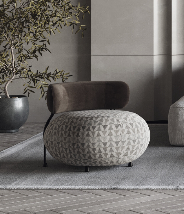 Round ottoman with gray geometric pattern and a dark brown curved backrest in a modern living room, next to a potted plant on a rug.