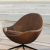 Brown egg shaped lounge chair on a balcony with the ocean in the background A modern swivel chair on a patterned outdoor rug