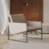 Modern beige lounge chair with a metal frame in a minimalist living room beside a light rug and brown wall panel behind