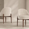 Two beige upholstered lounge chairs with dark wooden legs in a minimalist room