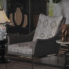 Grey armchair with geometric pattern cushions in a luxe living room with a lamp bronze elephant statue tall plants and a dark ornate cabinet in the background