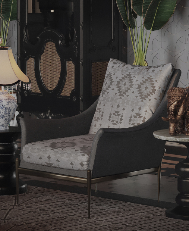 Grey armchair with geometric-pattern cushions in a luxe living room, with a lamp, bronze elephant statue, tall plants, and a dark ornate cabinet in the background.