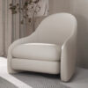 White modern upholstered armchair with rounded arms in a bright living room beside a tall plant and striped curtains