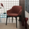Red upholstered lounge chair with black legs in a modern living space beside a glass side table and decorative vases